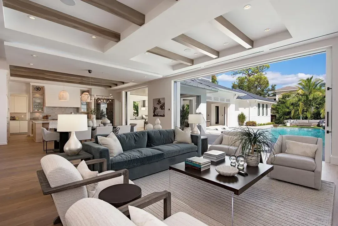 Luxurious open-concept living room with a pool view. Features a blue sofa, armchairs, and a kitchen.