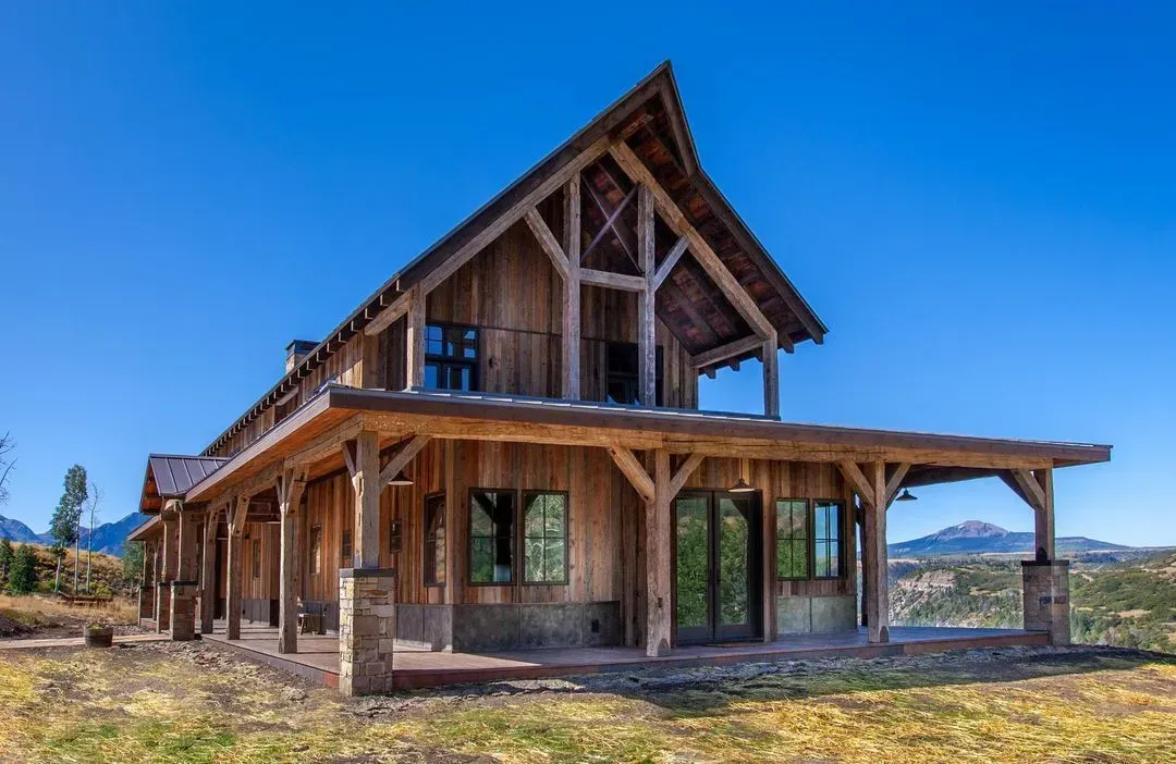 Rustic wooden house with porch and high gabled roof against a blue sky.