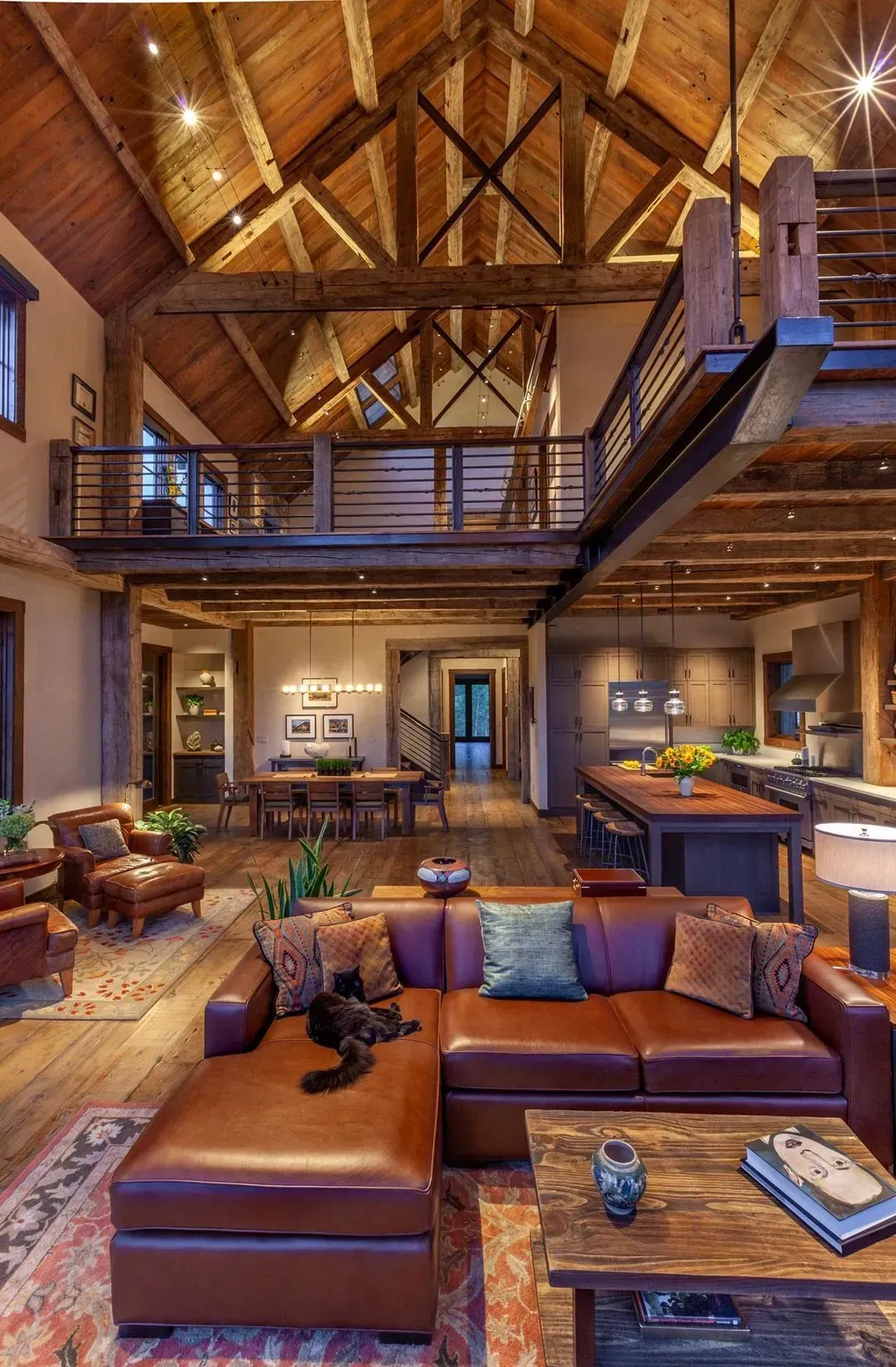Luxe rustic interior with wood beams, a leather sectional, and a loft, lit by warm lights.