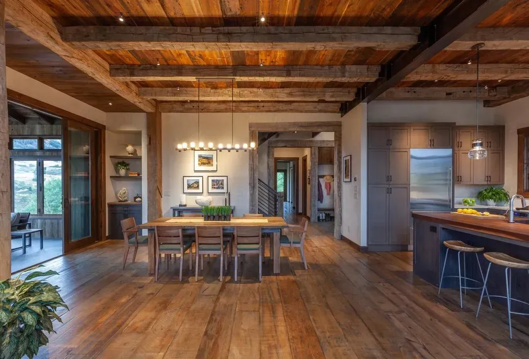Wooden-floored dining area with wood-beam ceiling. Table set for dining, kitchen in the background. Natural light.