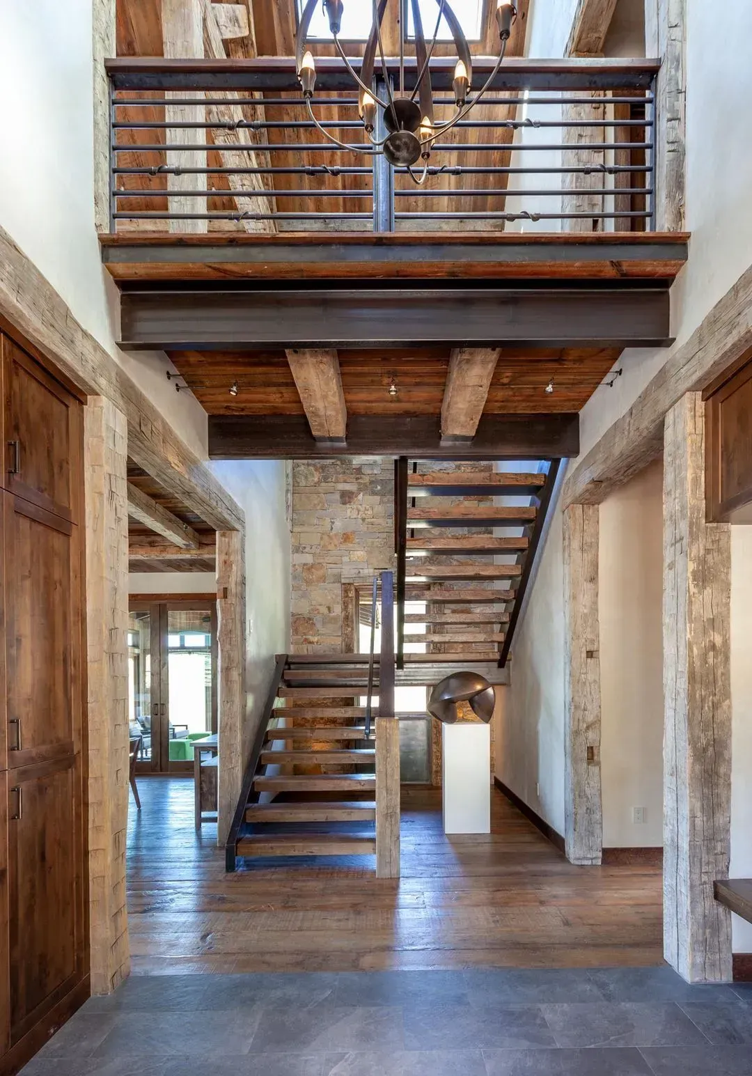 Rustic interior hallway with wooden beams, staircase, and balcony.