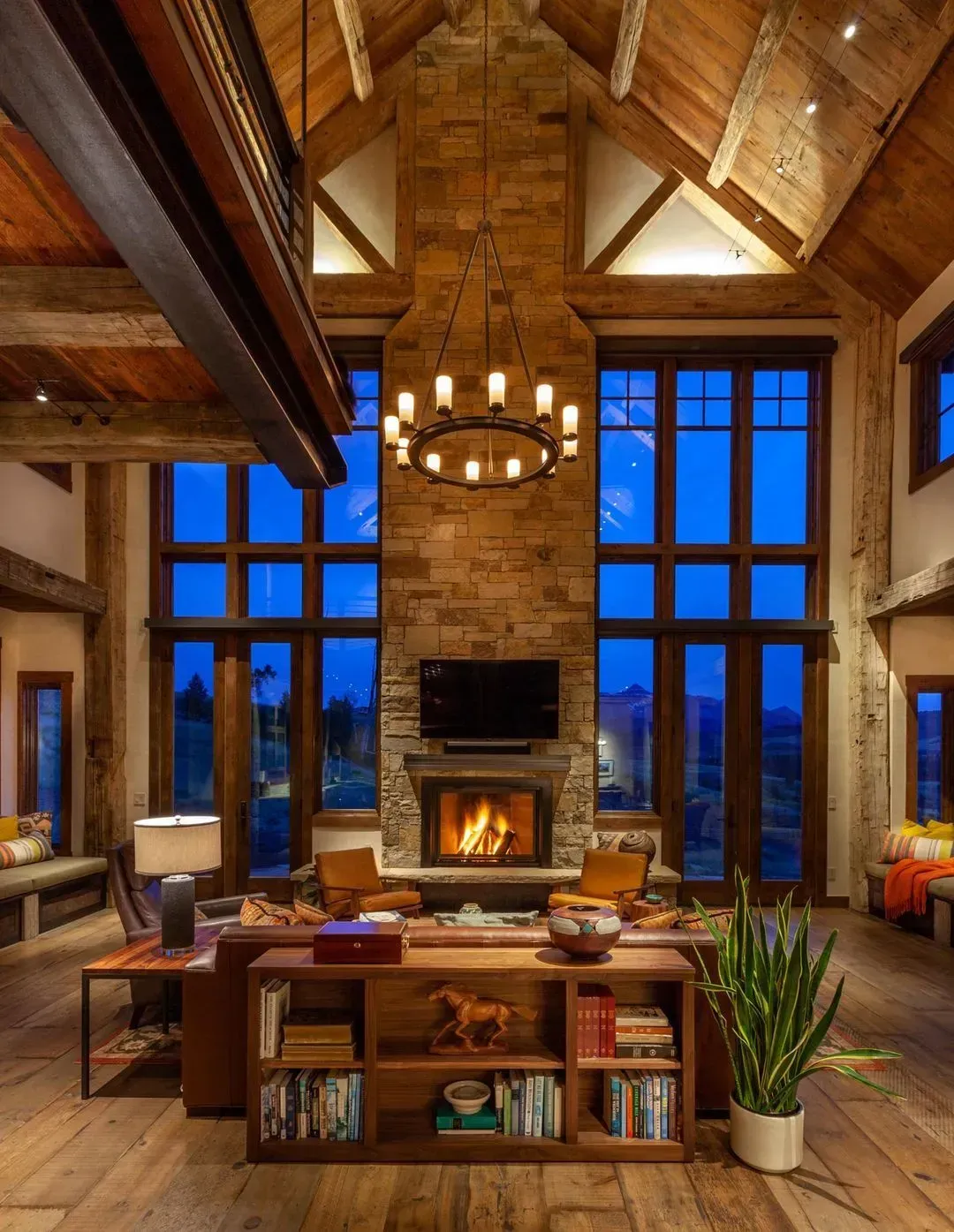 Rustic living room with a stone fireplace, large windows, and a chandelier.