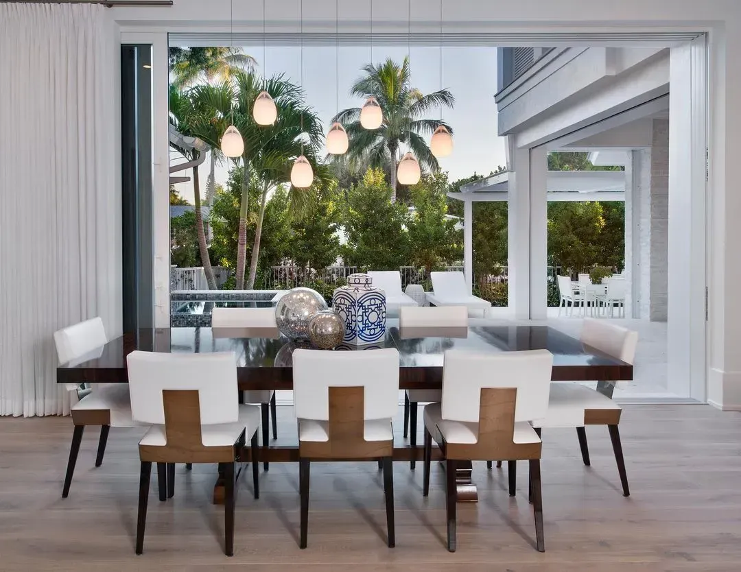 Dining room with dark wood table, white chairs, and view of tropical trees.