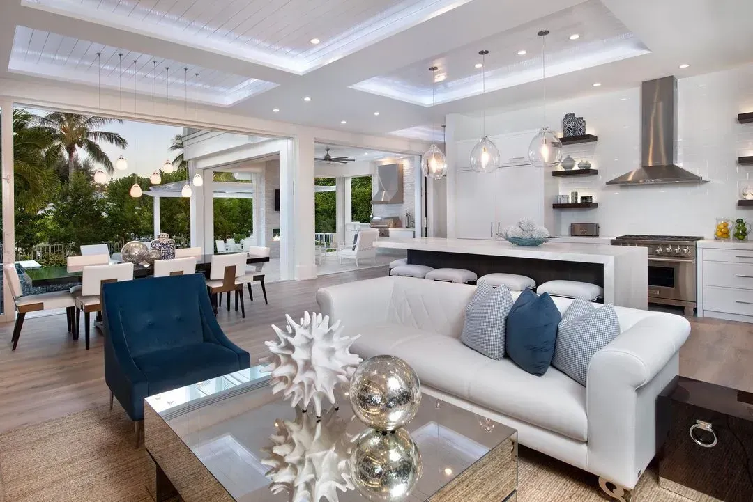 Bright, open-plan living room with white sofa, blue chair, and kitchen; sliding doors open to a dining area.