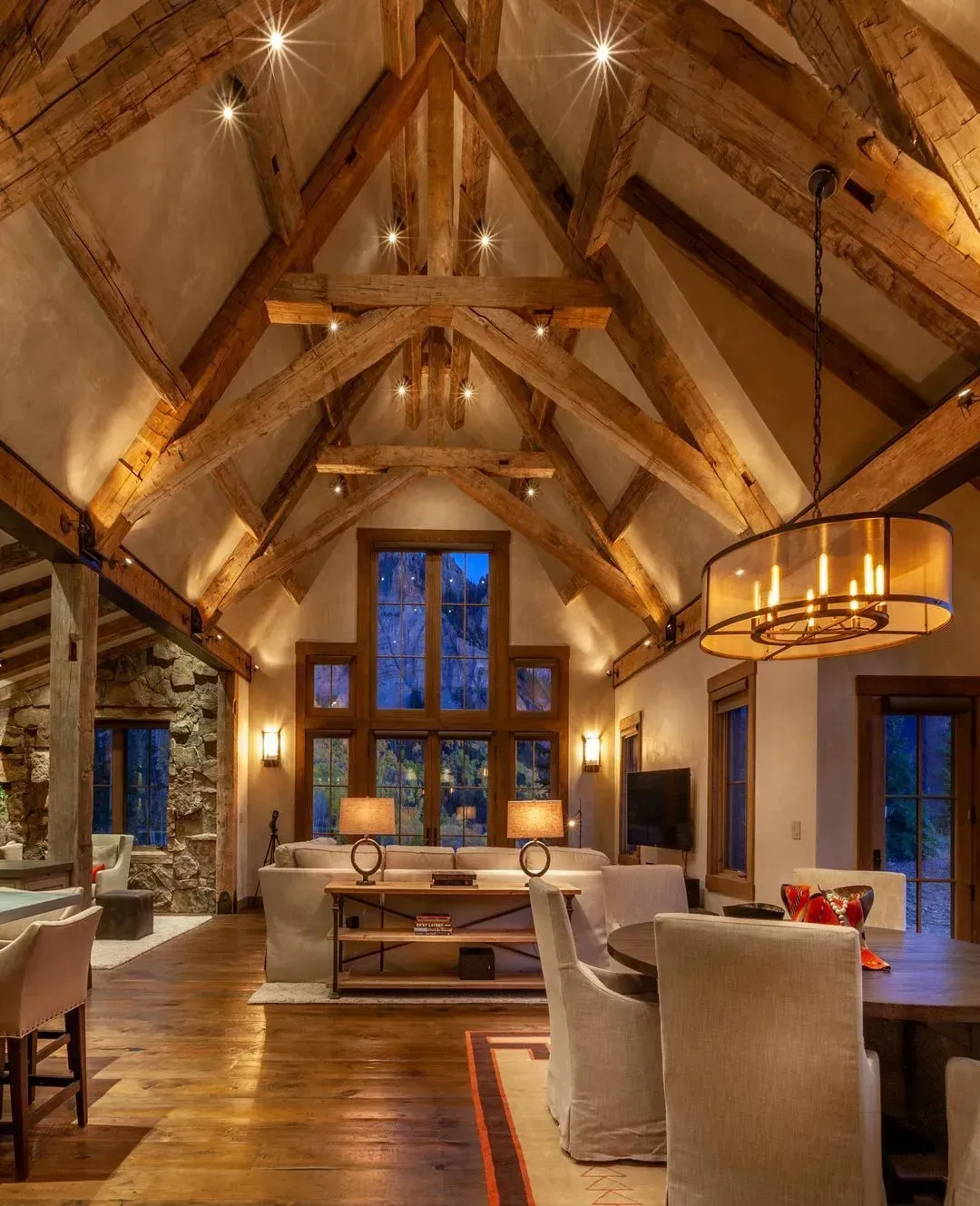 Rustic living room with wood beams, high windows, and chandelier.