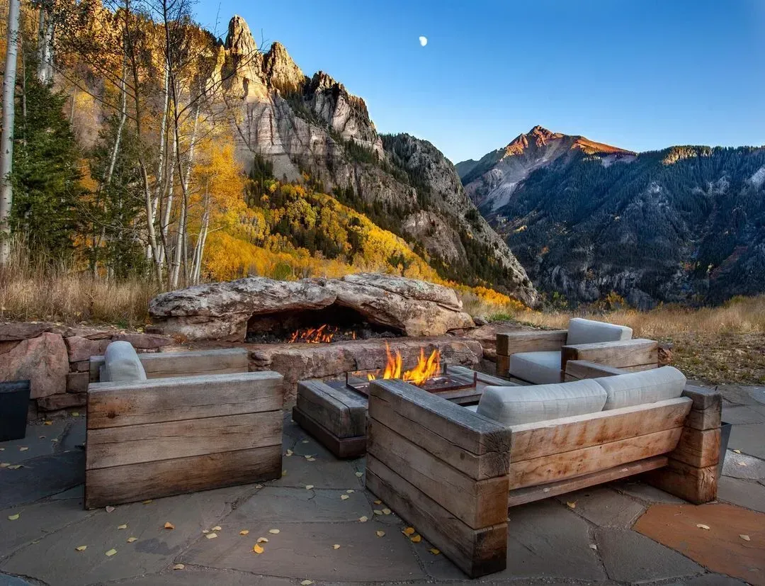 Outdoor seating area with fire pit, mountains in background, fall colors.