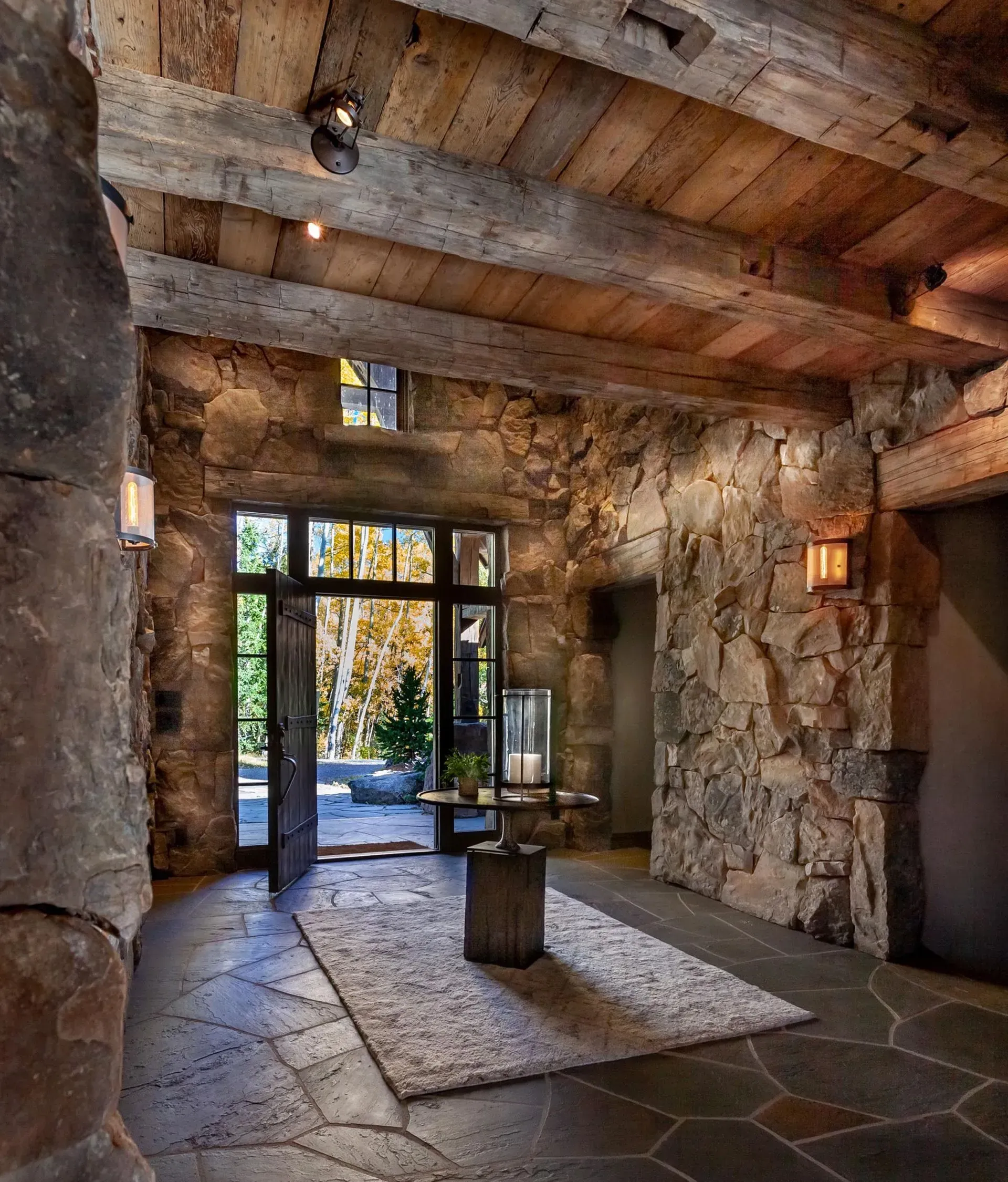 Stone entryway with wood ceiling beams, rug, and open door to outdoors.