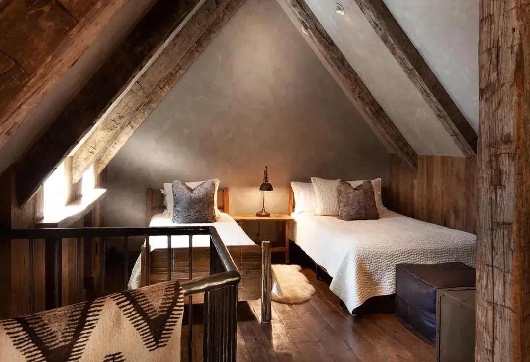 Cozy attic bedroom with two twin beds, wood beams, and a small table with a lamp.