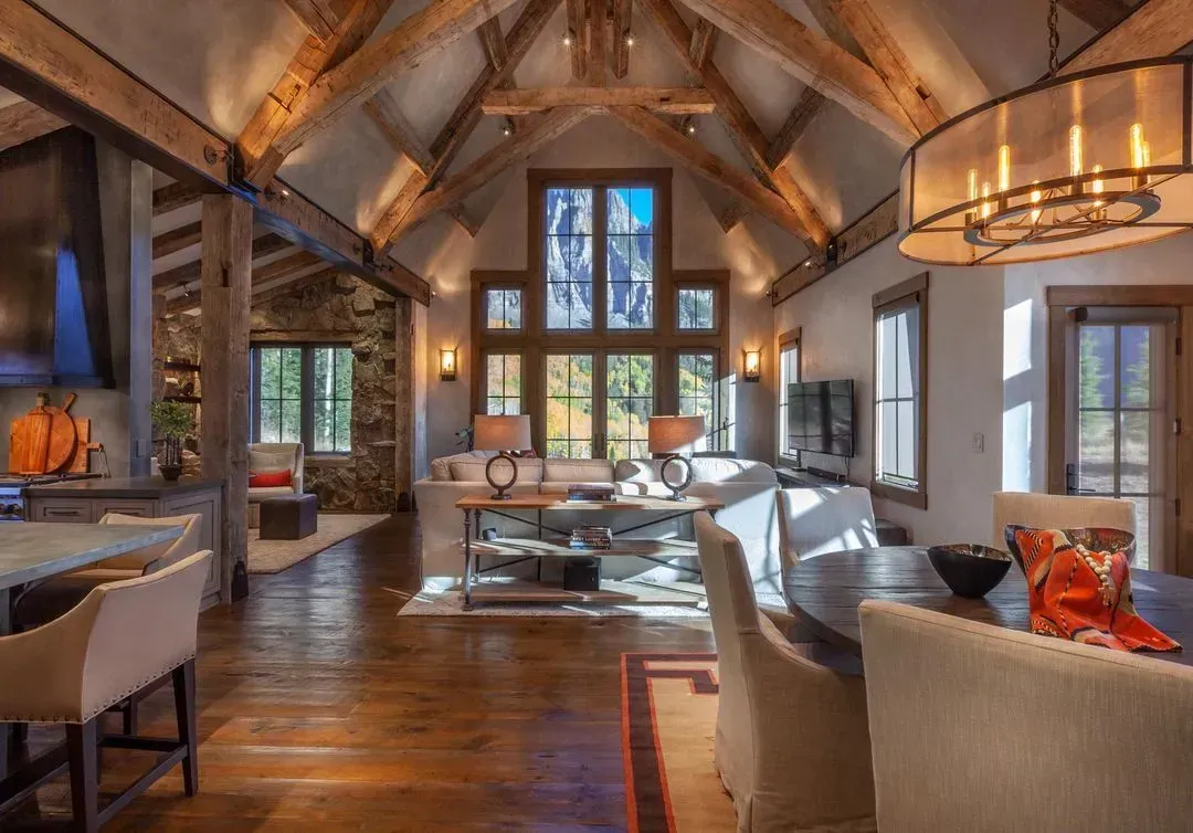 Spacious, rustic living room with wood beams, stone wall, and large windows.
