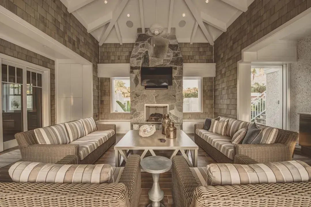 Spacious living room with stone walls, vaulted ceiling, and wicker furniture facing a fireplace.