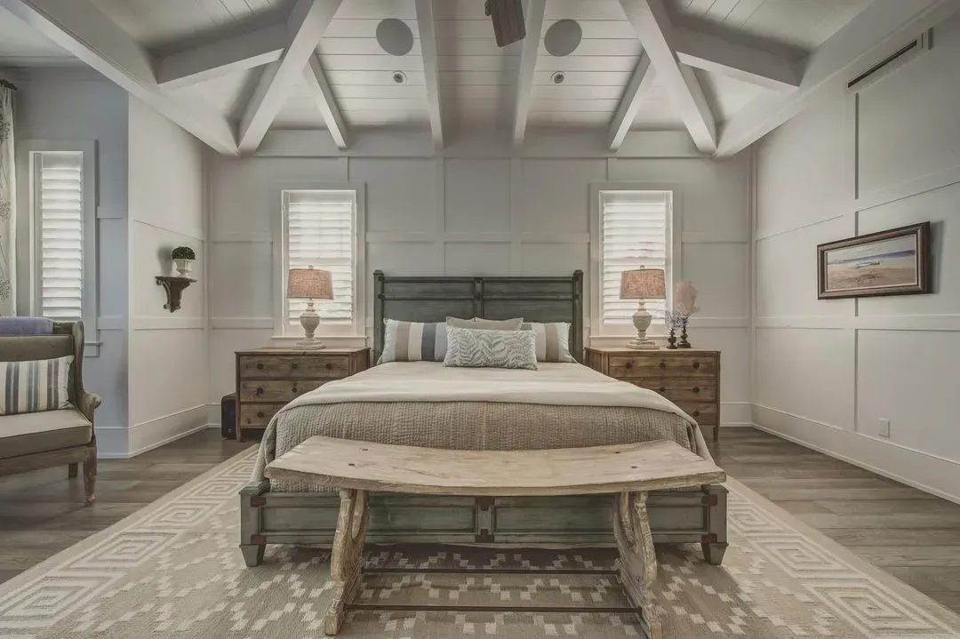 Bedroom with light wood furniture, white walls, and a wood beamed ceiling.
