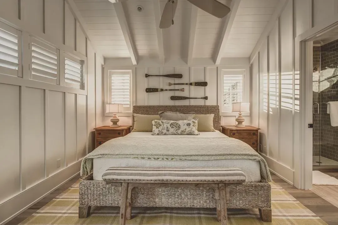 Bedroom with white paneling, bed, nightstands, oars, and a bench, with a doorway to the right.