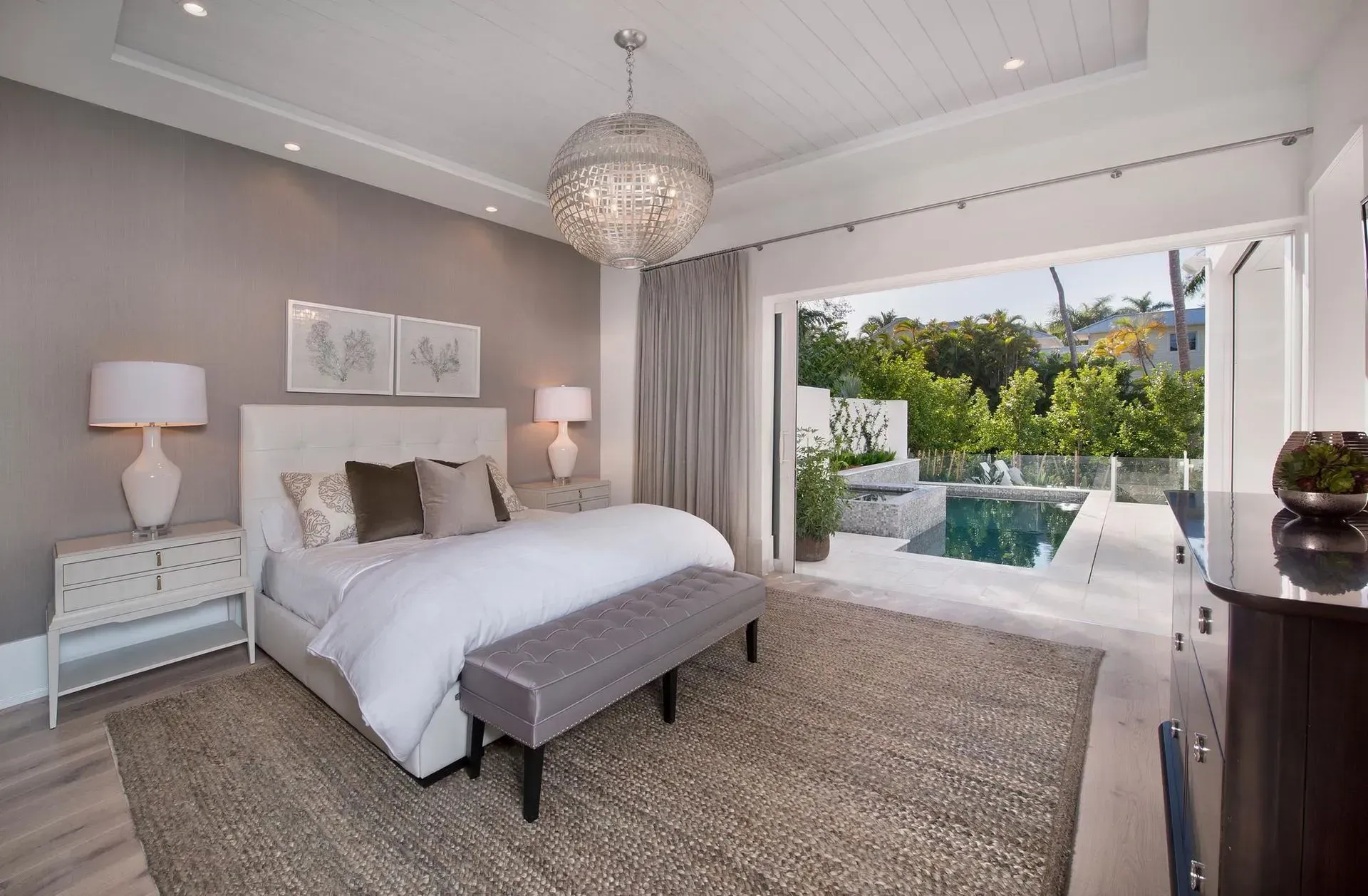 Bedroom with white and gray decor, opening to a pool area with trees.