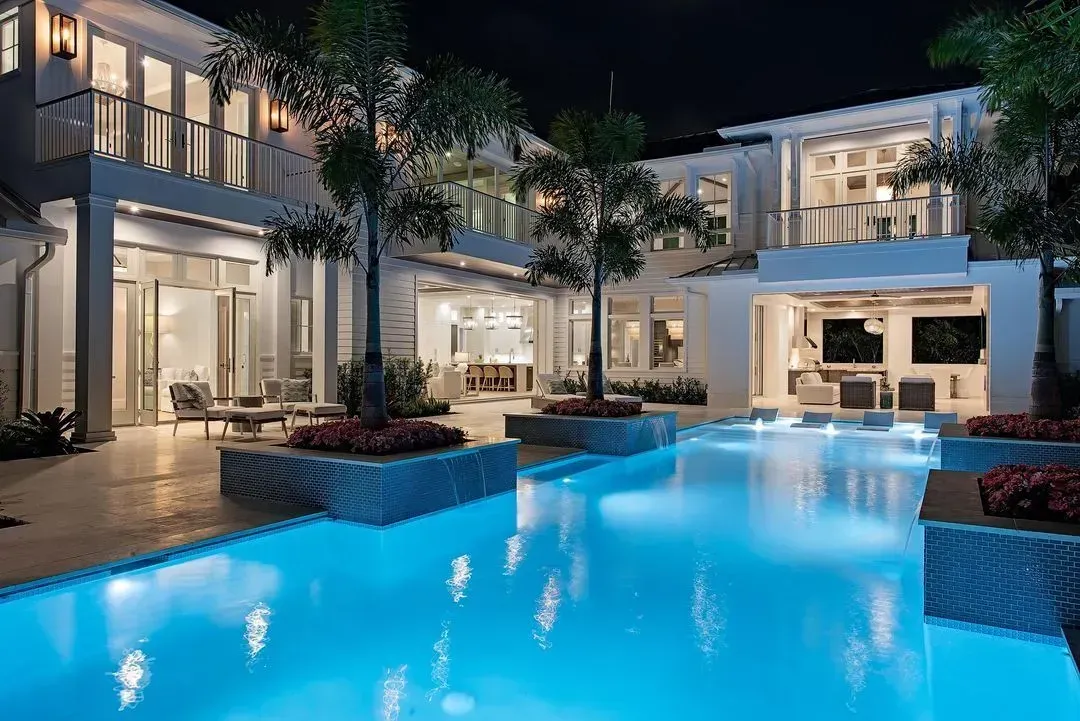 Luxury home with a glowing blue pool at night.