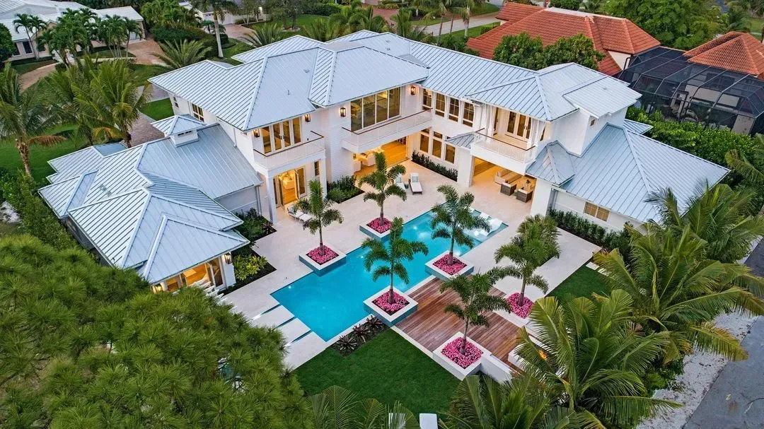 Luxury white mansion with a pool, palm trees, and green lawn.