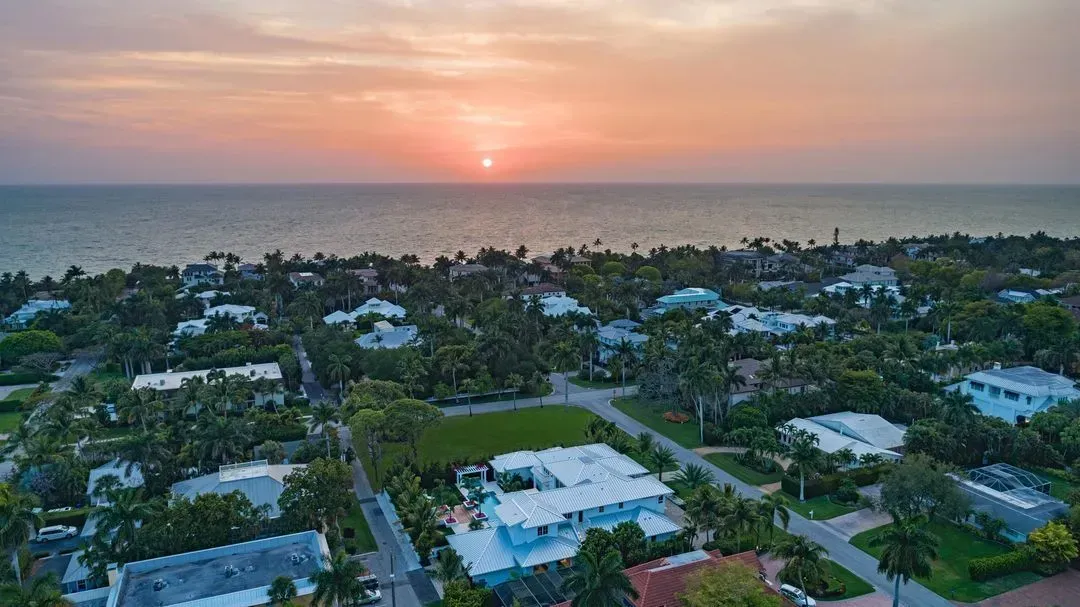 Sunset over ocean and coastal homes with palm trees.