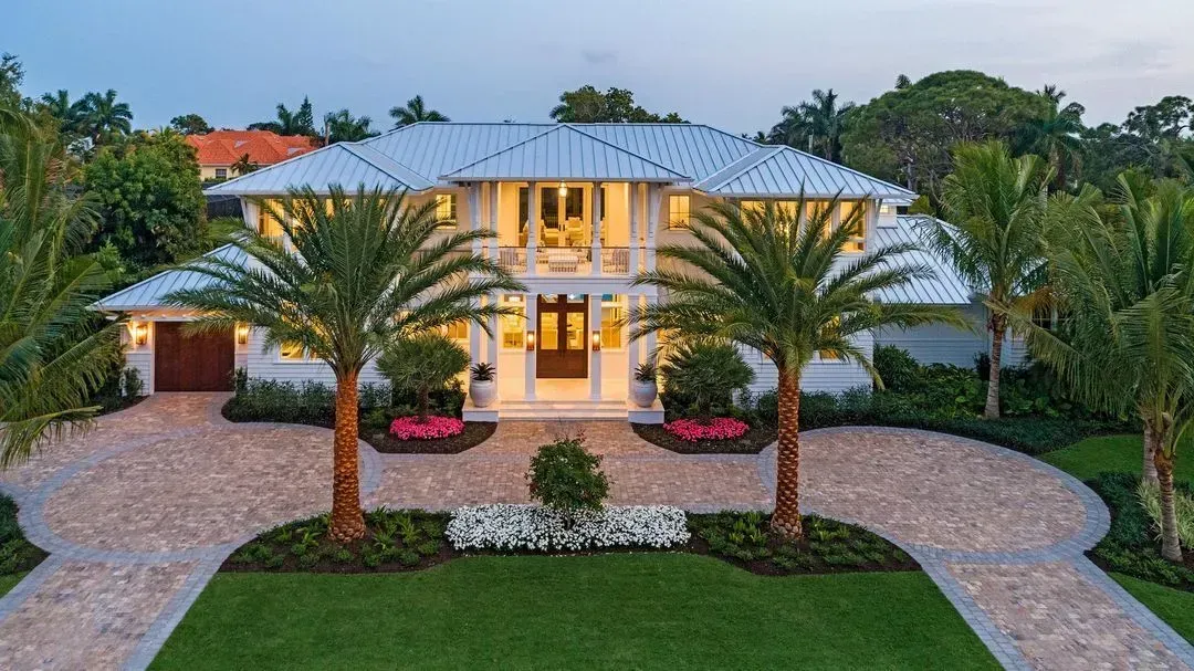 Two-story white house with light stone driveway and palm trees in front.