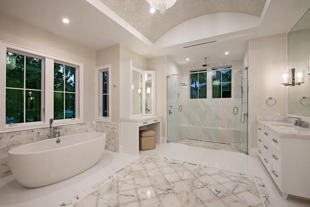 Spacious, luxurious bathroom with freestanding tub, marble floors, glass shower, and vanity under patterned ceiling.