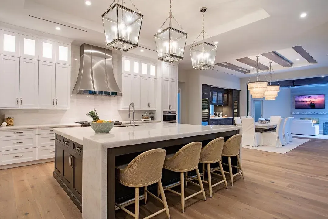 Spacious kitchen with island, seating, white cabinets, and pendant lights. Open to dining area and living room.