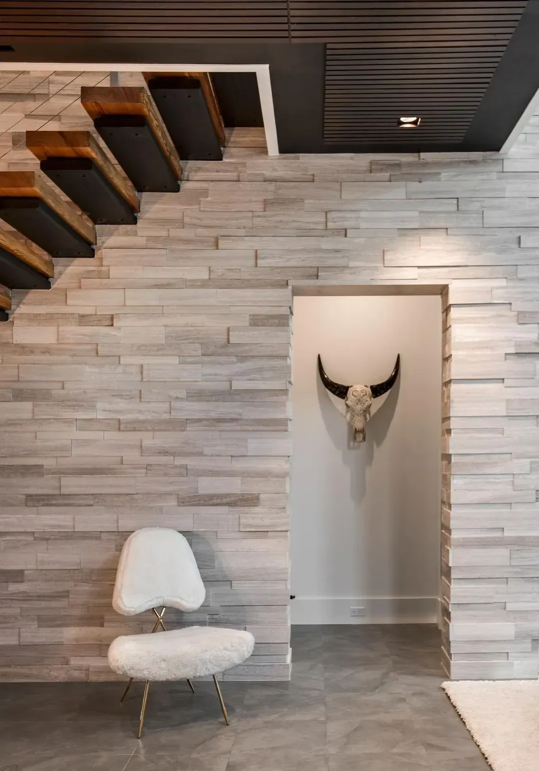 Modern interior with stacked stone wall, floating staircase, white chair, and skull decoration.