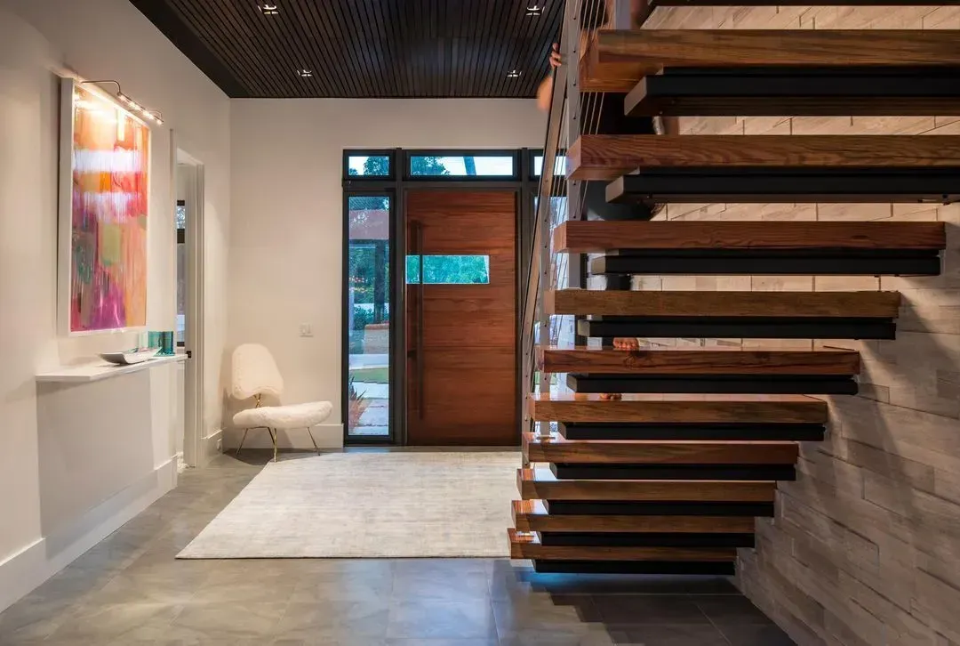 Modern home entry with wooden staircase, front door, artwork, and white walls.
