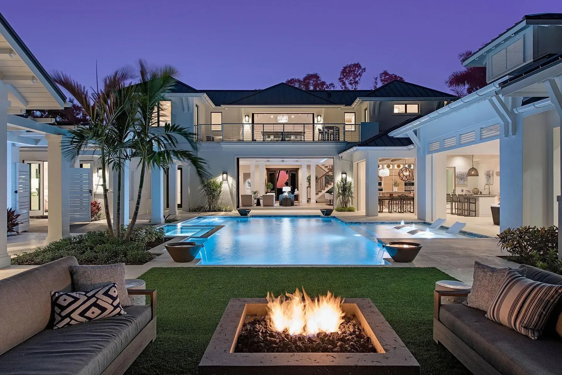 Luxury home exterior with pool, fire pit, and outdoor seating at dusk.