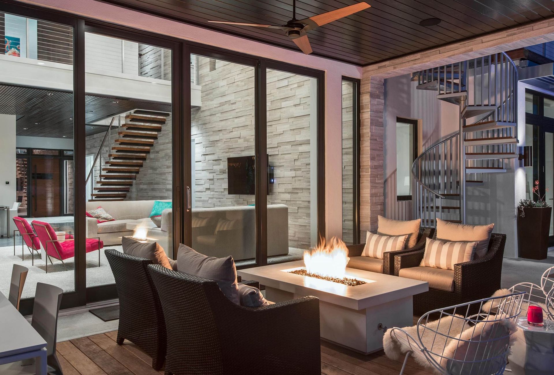 Outdoor patio with fire pit, seating, and spiral staircase leading to upper levels of a modern home.
