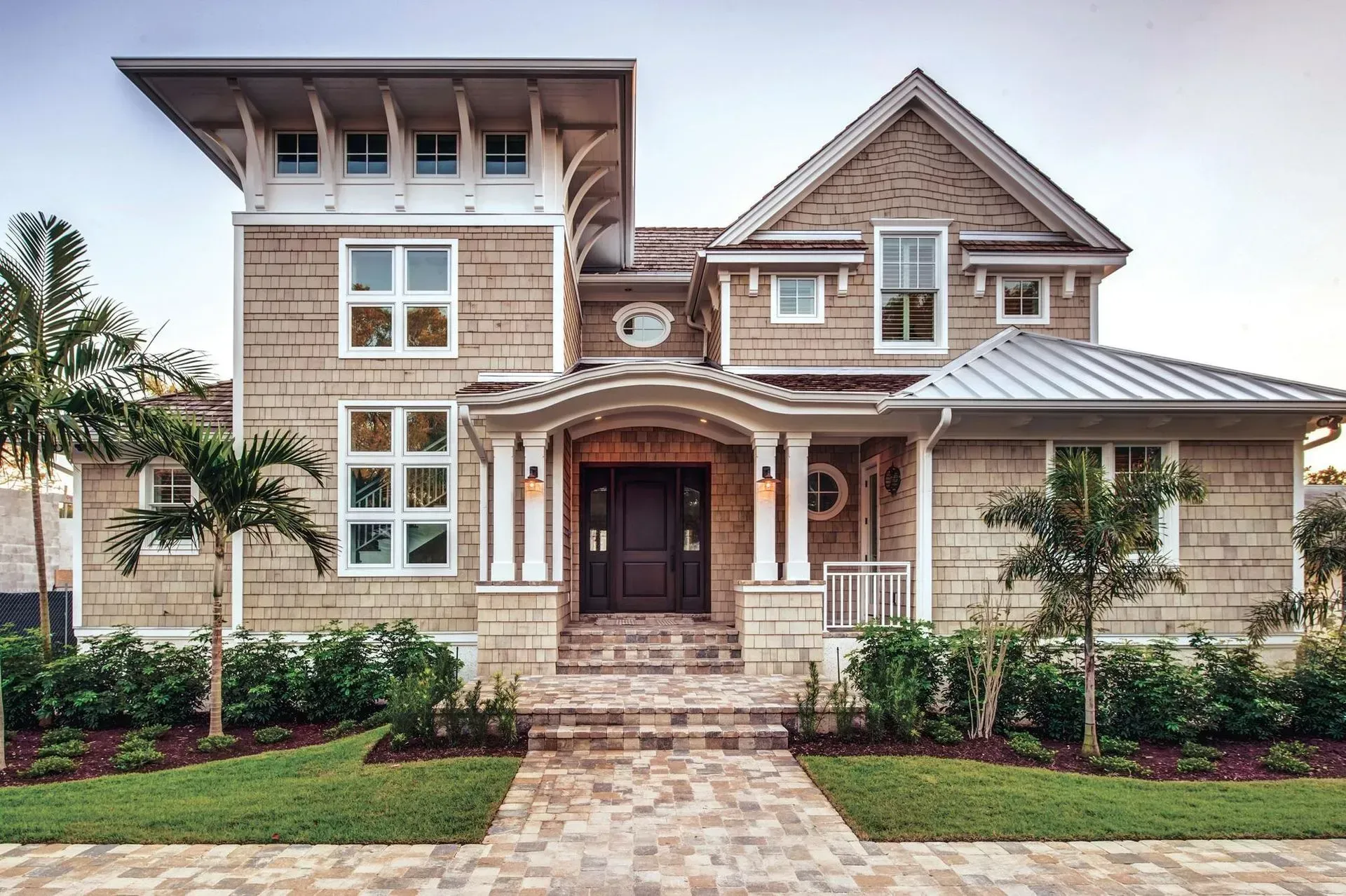 Two-story coastal home with light tan siding, a brown door, and a brick pathway.