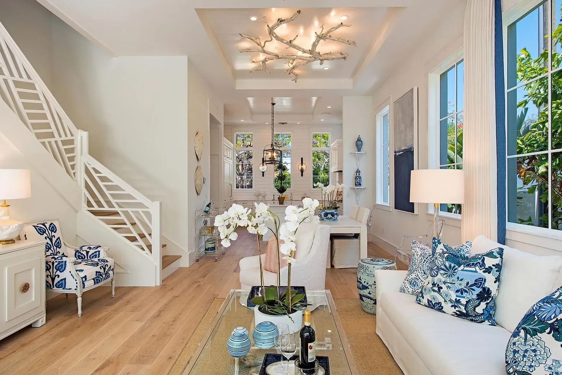 Bright living room with white walls, blue accents, staircase, and a view to dining area.