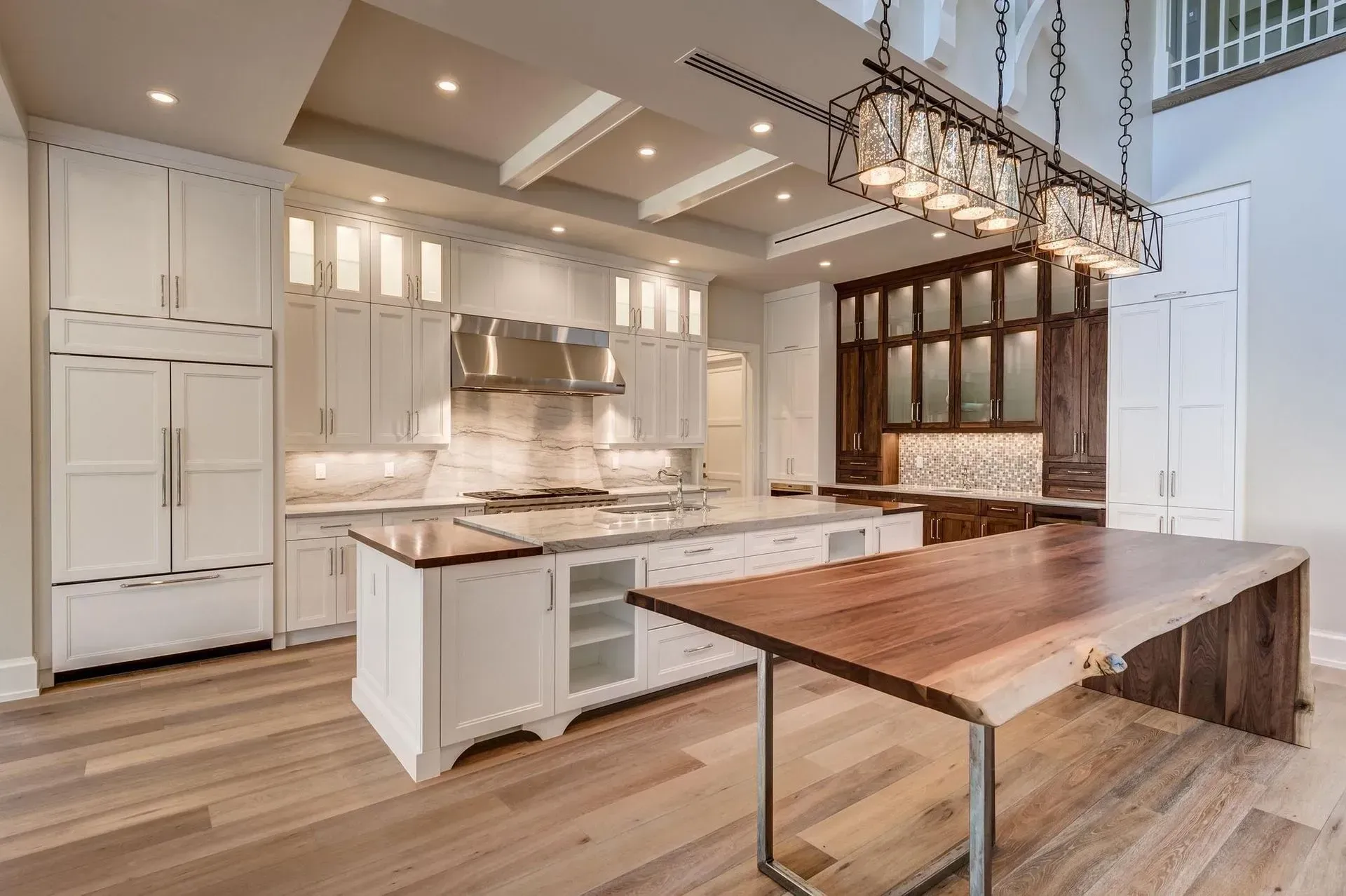 Spacious kitchen with white cabinets, island, and wooden table, brown accents, and light wood floors.