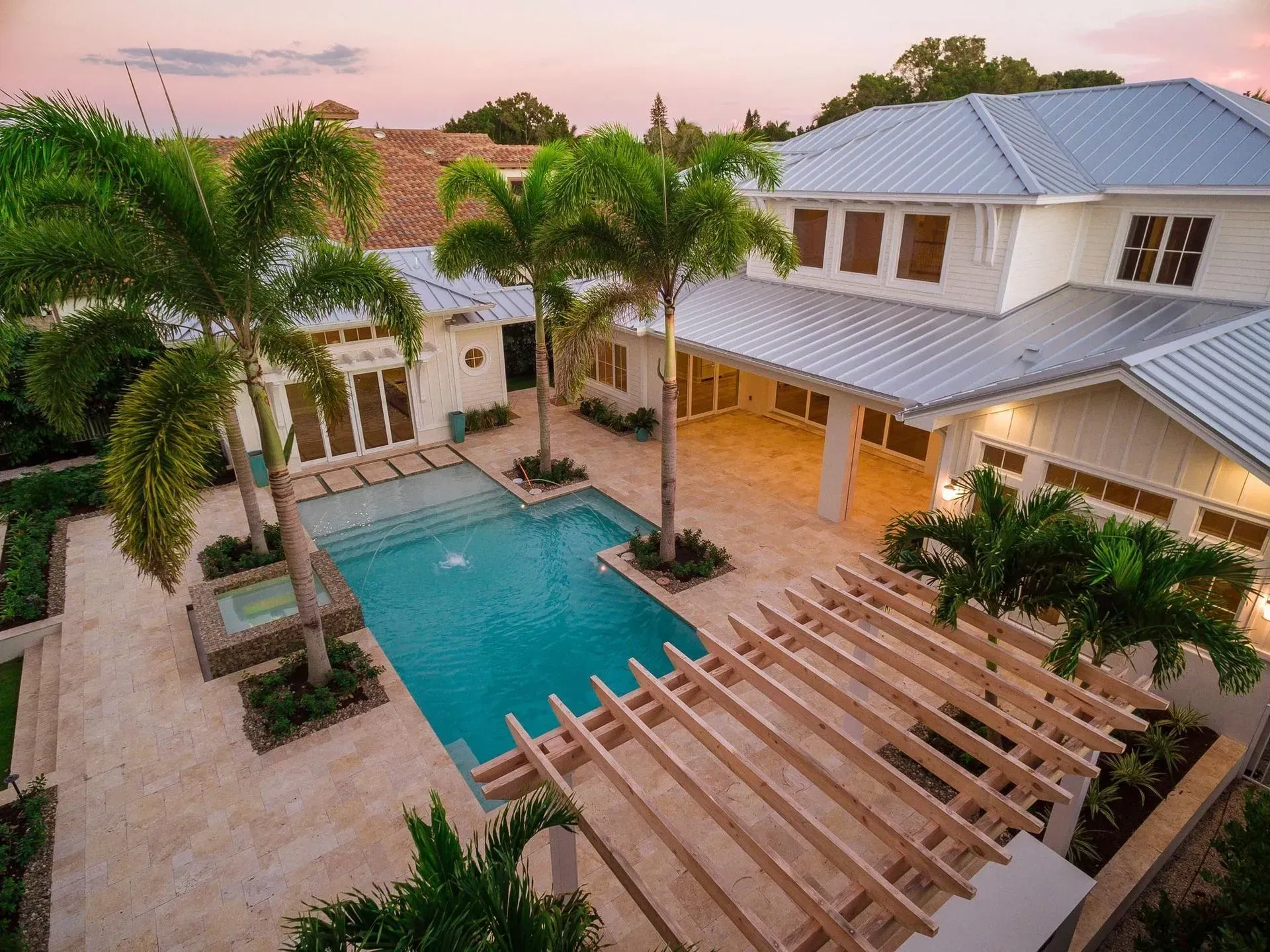 Upscale white house with pool and palm trees in courtyard.
