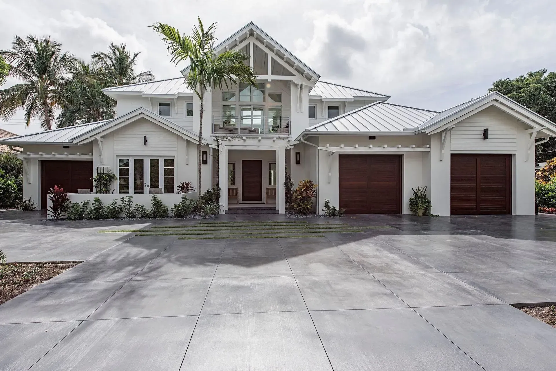 White two-story house with dark brown garage doors, gray driveway, and palm trees.