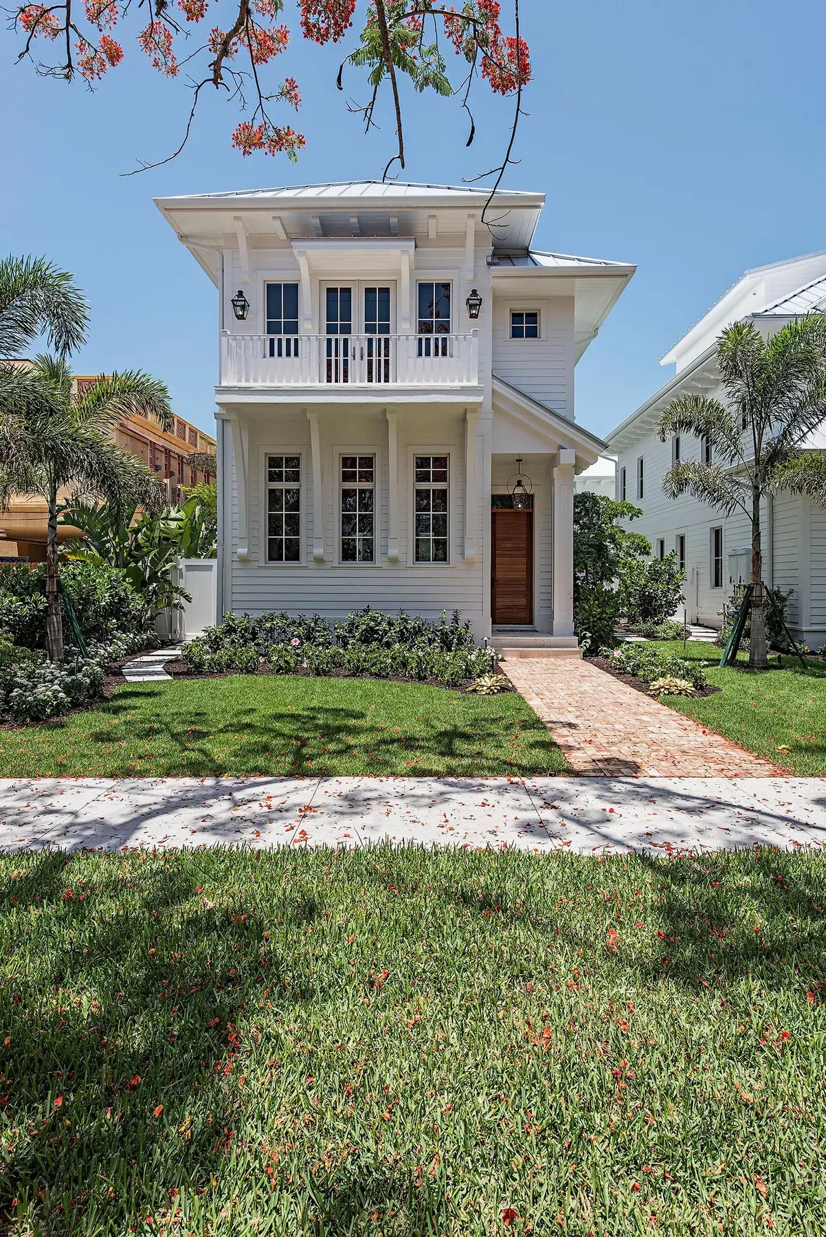 White two-story house with balcony, wooden door, brick path, green lawn, sunny day.