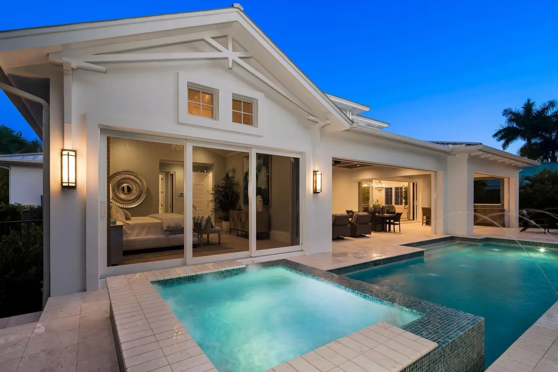 Backyard with pool, hot tub, and house; evening blue sky.