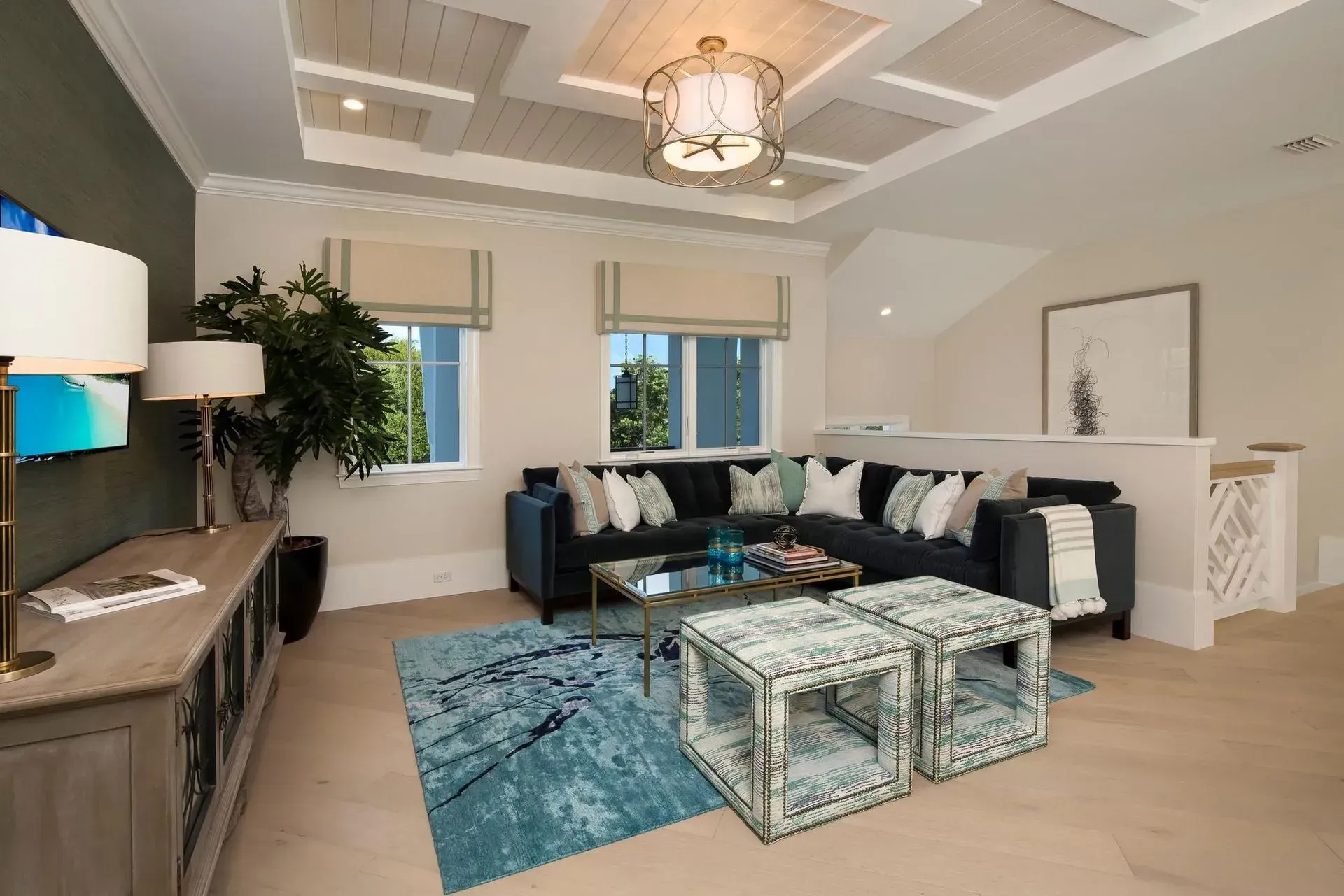 Living room with blue sectional, teal rug, and ottomans, neutral walls, and a coffered ceiling.