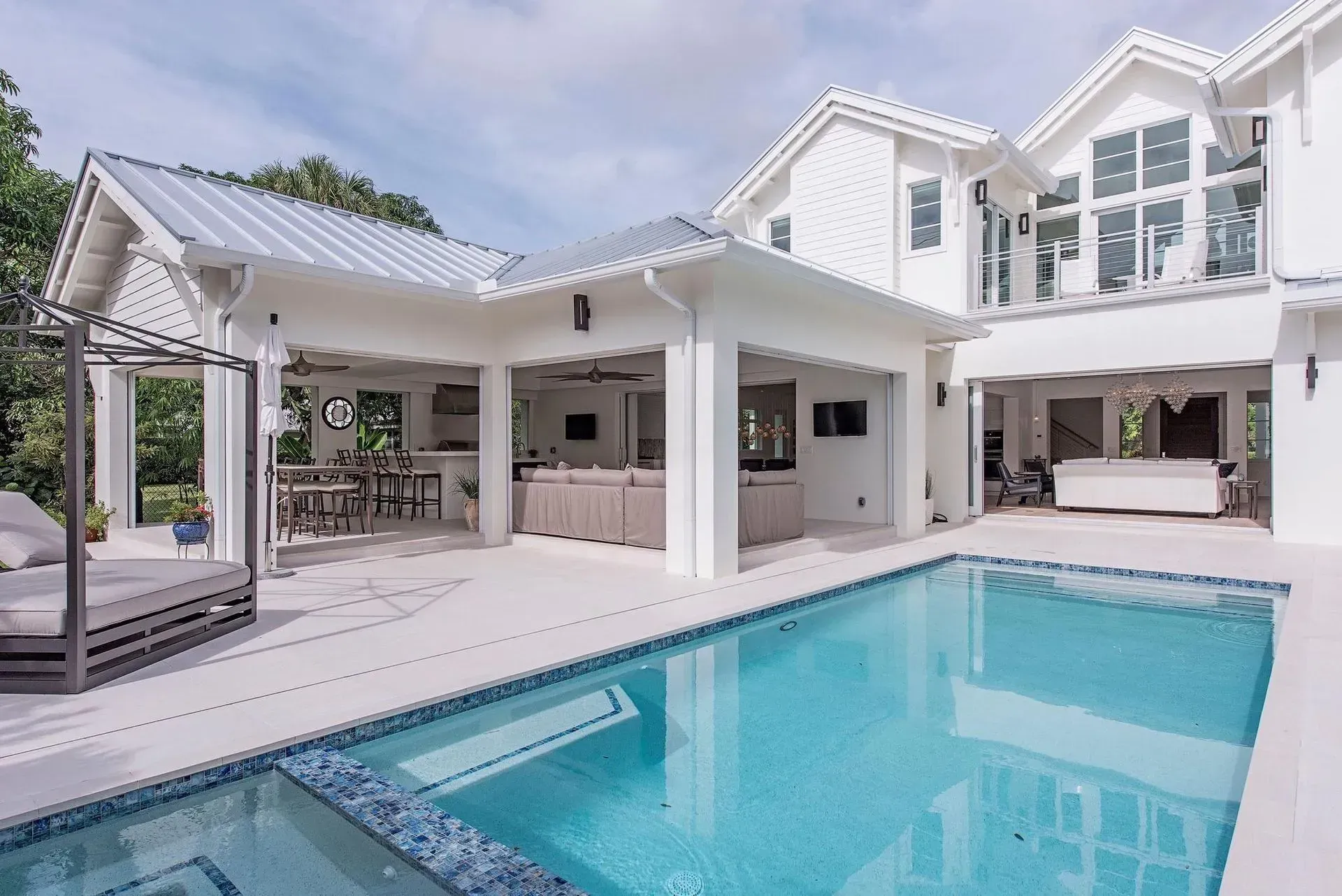 Pool area of a white house with a pool, outdoor kitchen, and patio furniture.