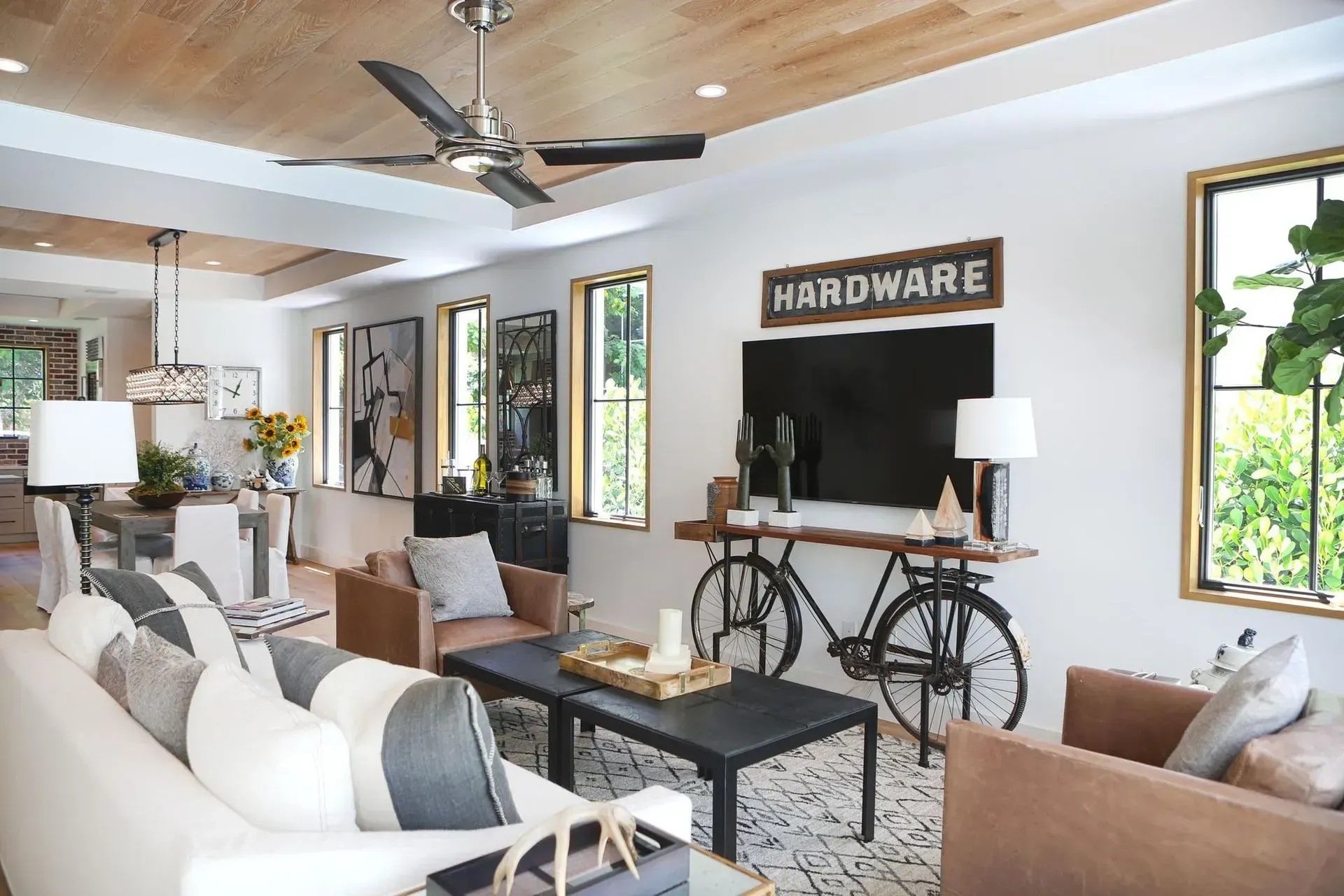 Living room with white walls, wood ceiling, dark TV, bicycle table, and black and white patterned floor tiles.