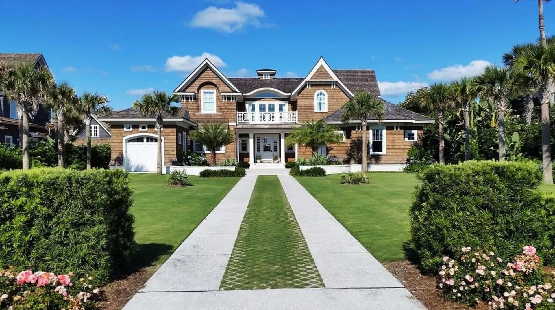 Luxurious home with brown siding, white trim, and a long walkway on a sunny day.