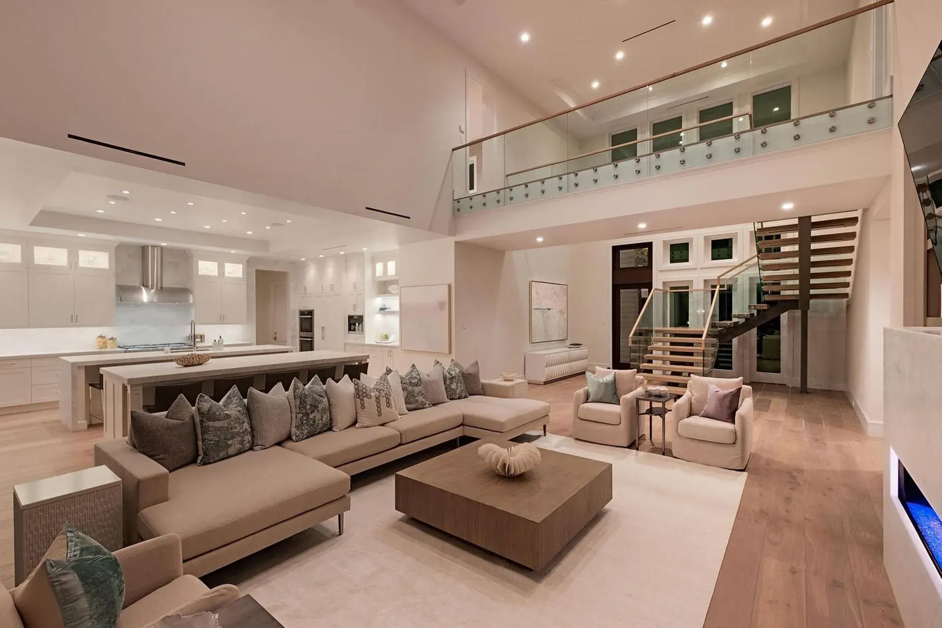 Modern living room with open kitchen, neutral tones, and a second-story balcony.
