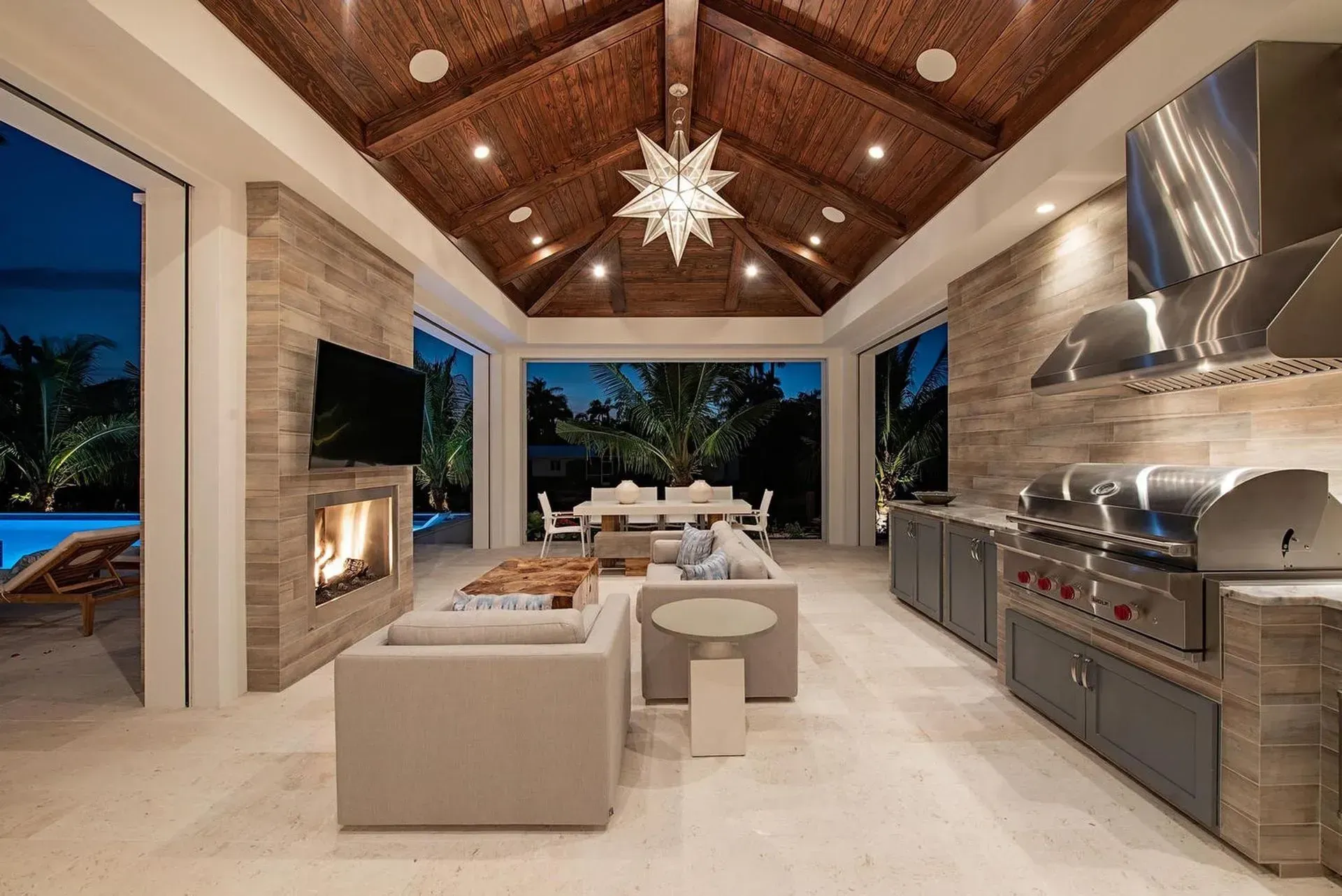 Outdoor kitchen and living space with a fireplace, grill, and seating area.