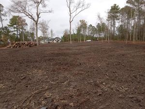 A muddy field with trees in the background and a house in the background.