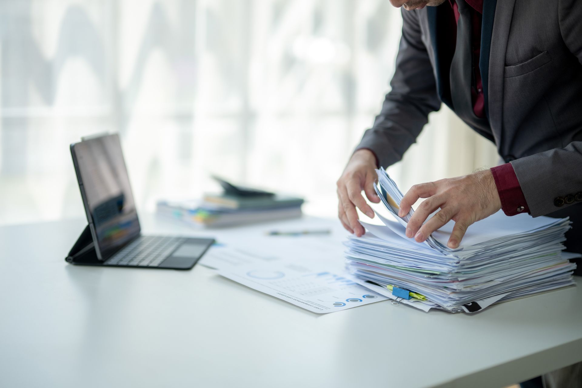 Person sorting a stack of documents beside an open laptop on a desk