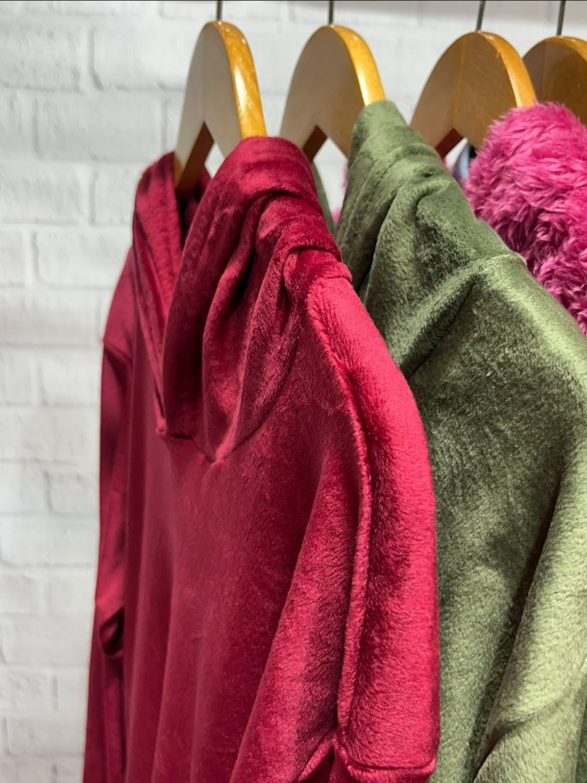 Mujer con sudadera roja, mano en el bolsillo, sonriendo; vistiendo leggings negros.