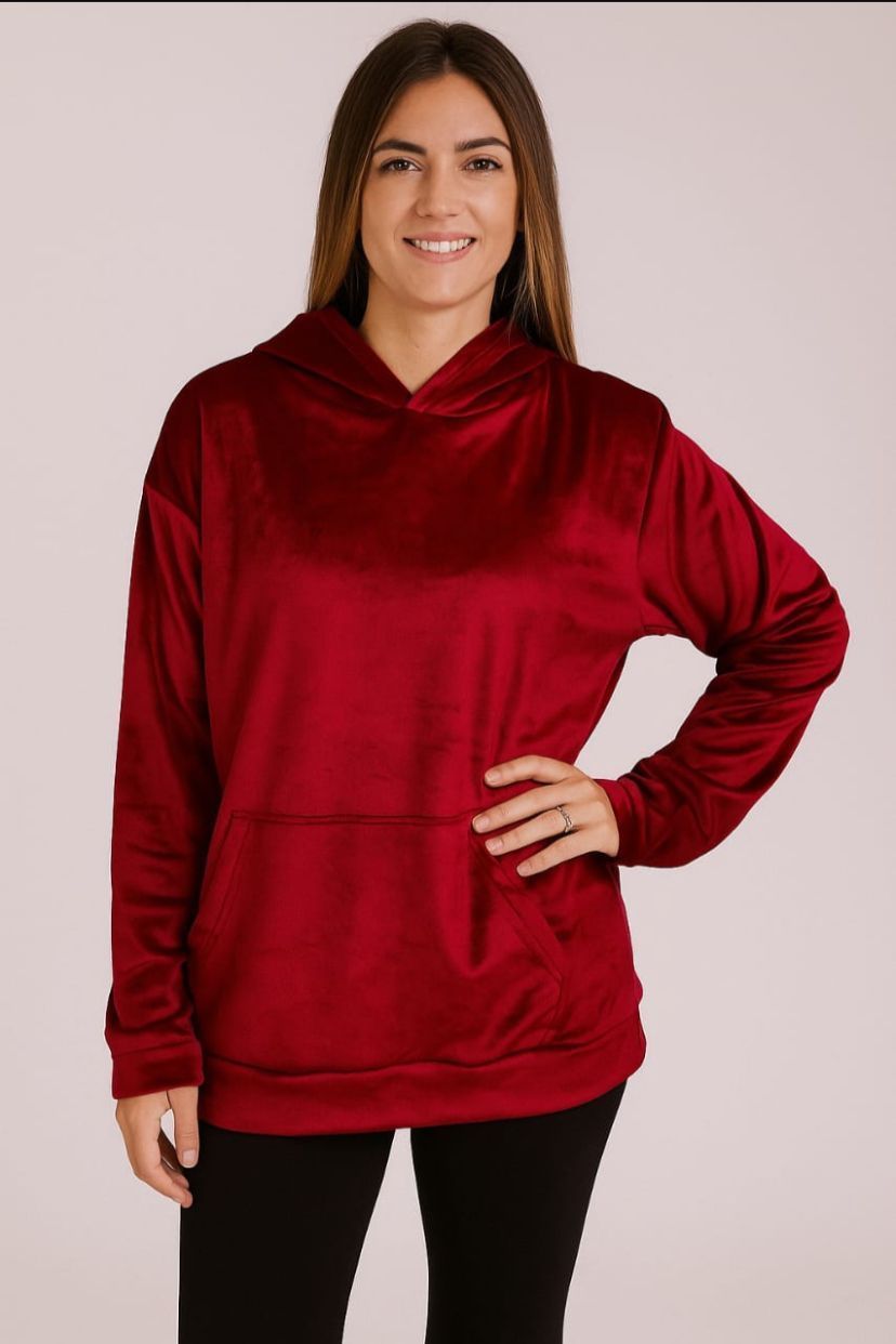 Mujer con sudadera roja, mano en el bolsillo, sonriendo; vistiendo leggings negros.