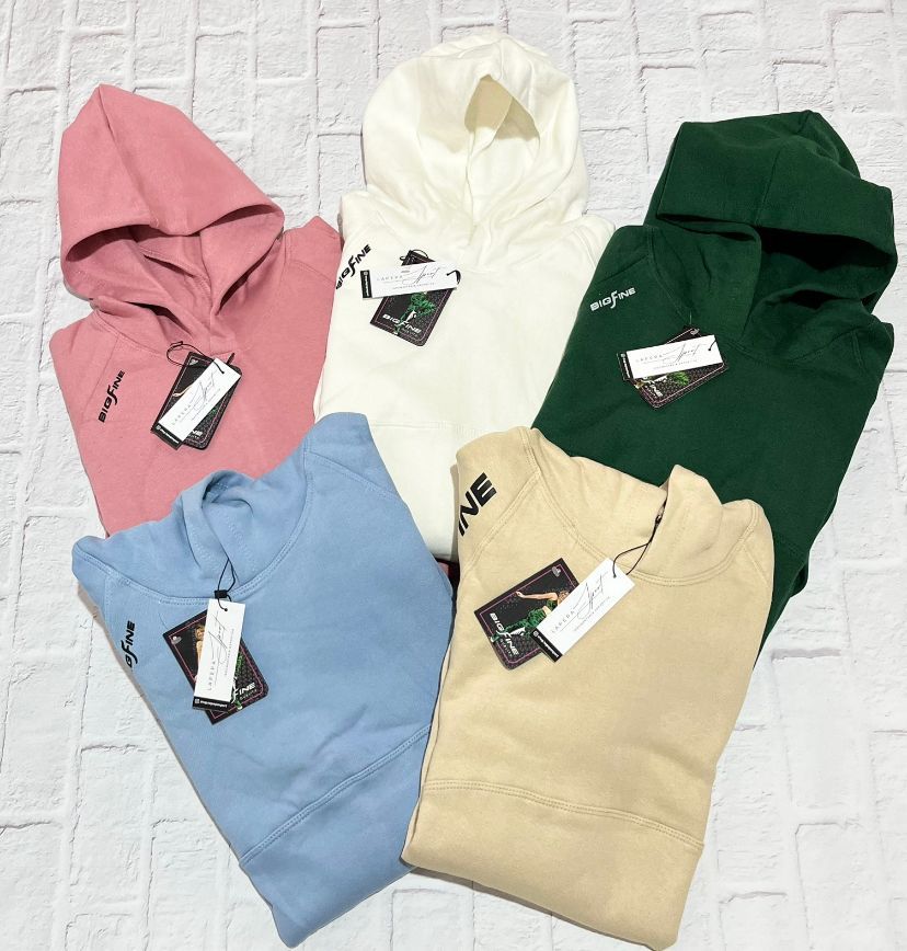 Mujer que lleva una sudadera blanca larga, con la mano en la cadera y una etiqueta en el pecho.