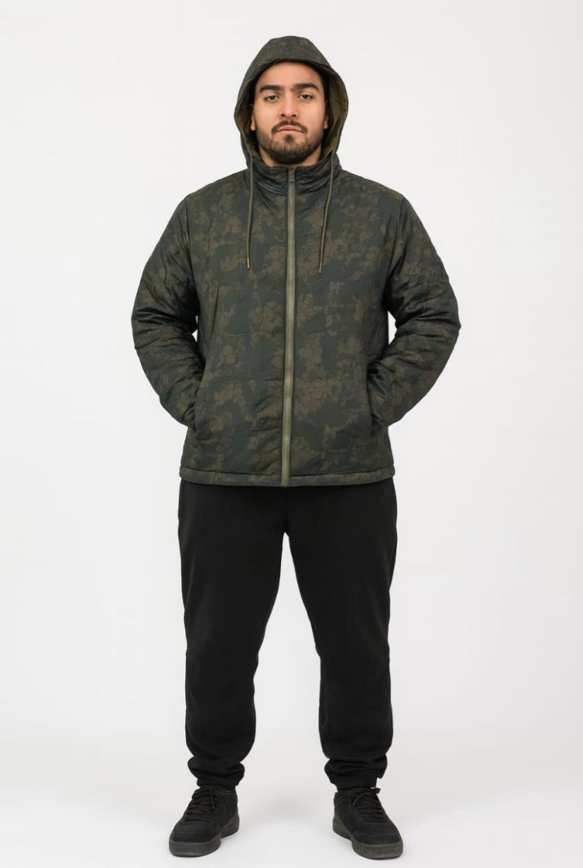 Hombre con una chaqueta de camuflaje con capucha y pantalones deportivos negros, de pie con las manos en los bolsillos.