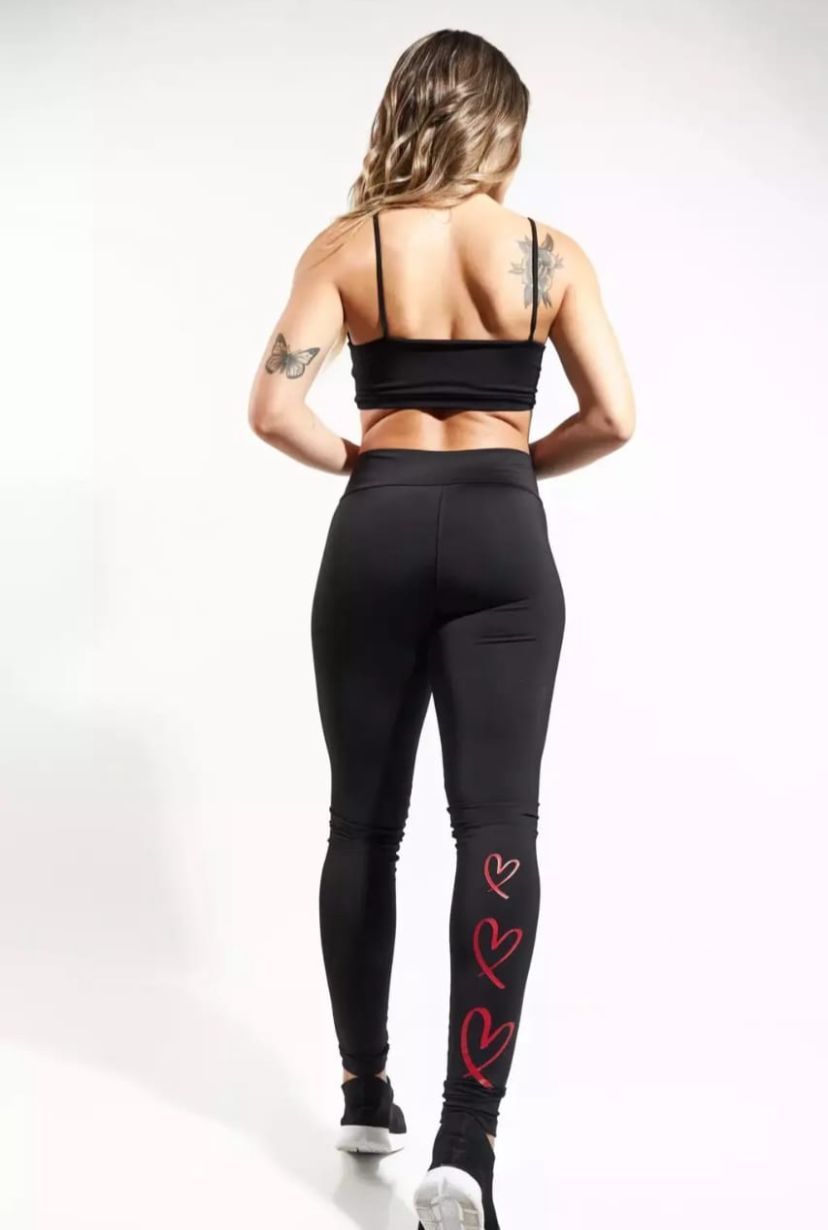 Una mujer con ropa deportiva negra sonríe, mirando por encima del hombro. Corazones rojos en el tobillo. Zapatillas blancas.