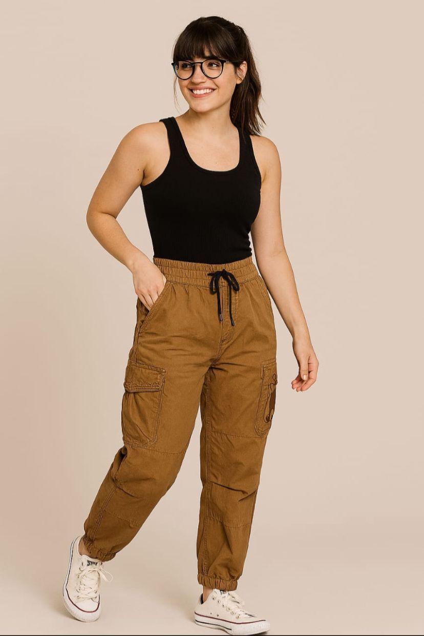 Mujer con camiseta negra y pantalones cargo marrones, sonriendo, con gafas y zapatillas blancas.