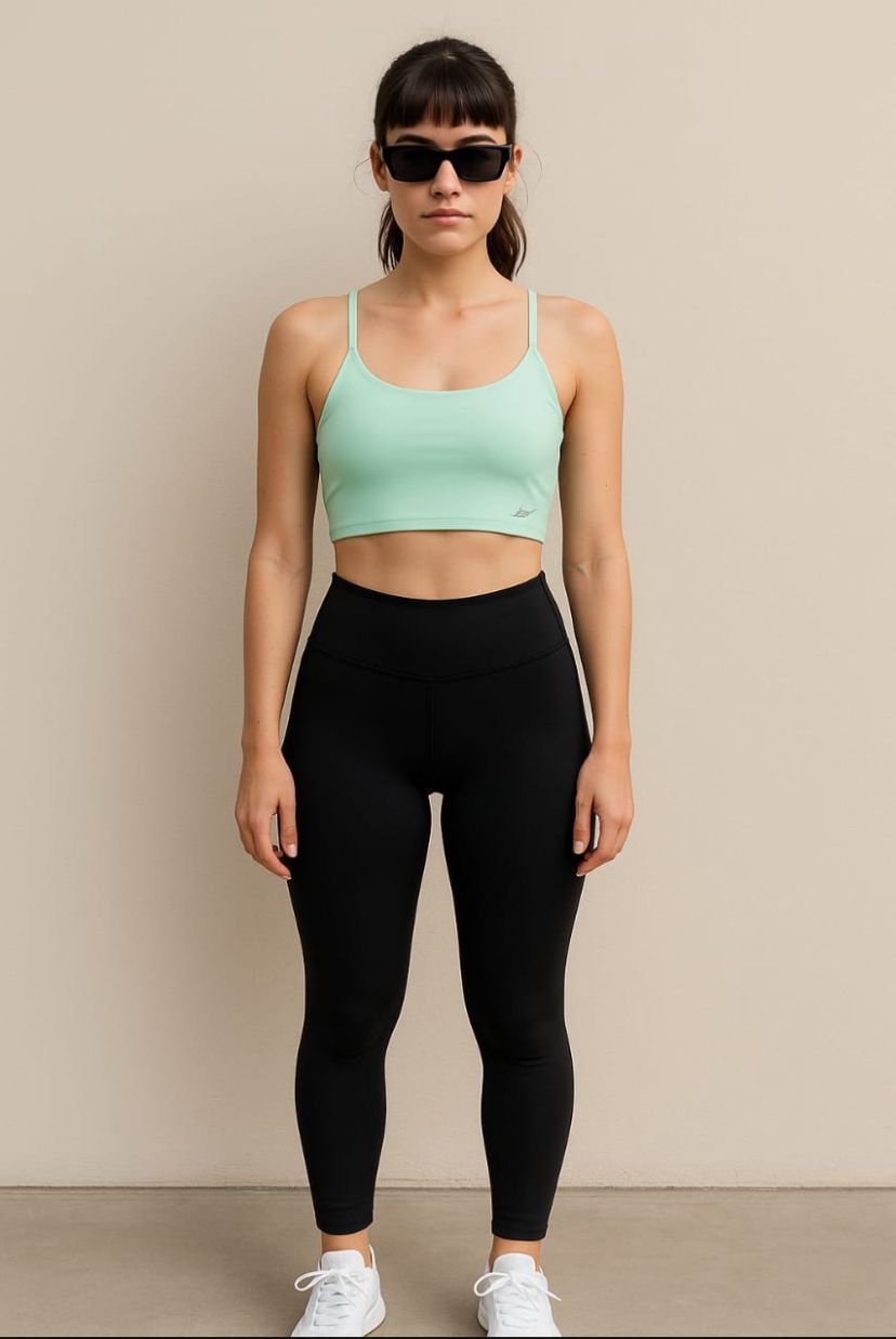 Mujer con top corto verde menta, leggings negros y zapatillas blancas, y con gafas de sol.