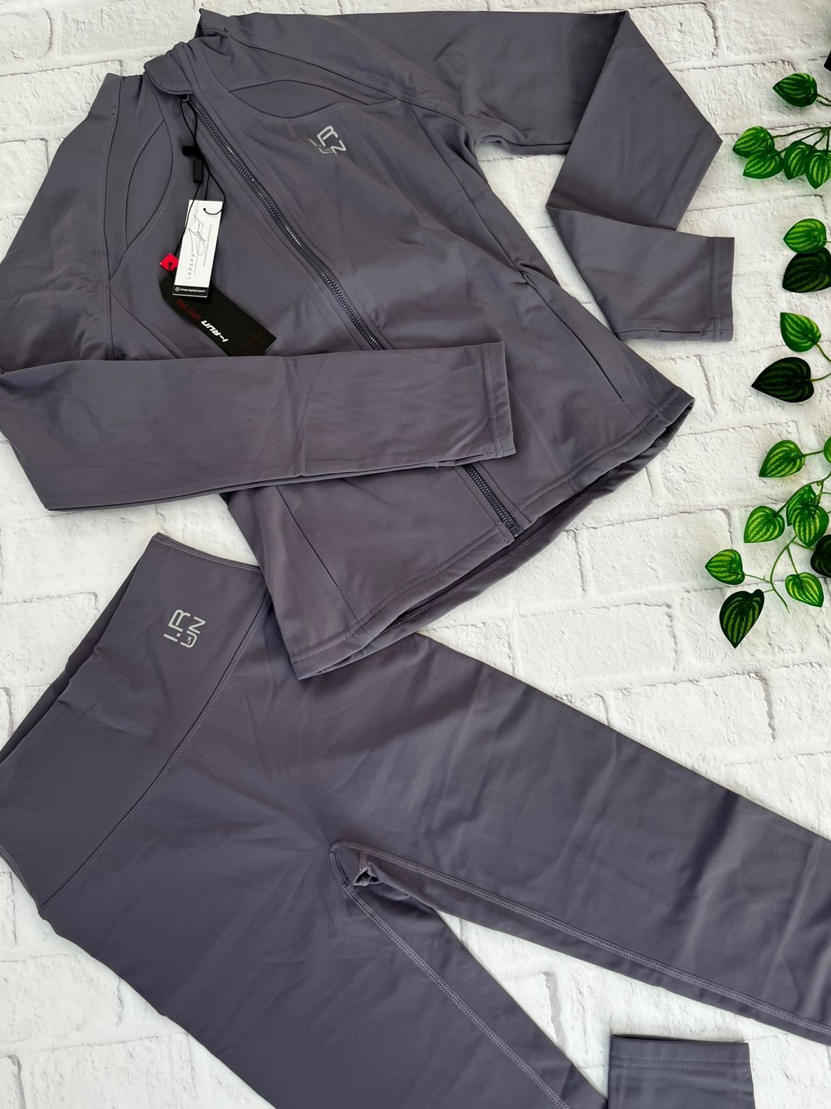 Mujer vestida con ropa deportiva gris, de pie, con una chaqueta con cremallera y mallas, con zapatillas blancas.